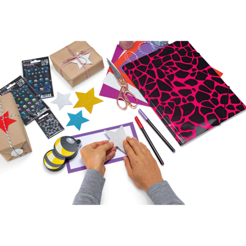 Hände gestalten eine Stern-Dekoration mit buntem Papier, Scheren, Stiften und verpackten Geschenken auf einem Tisch.