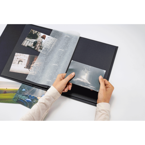 Eine Person hält ein Foto und blättert durch ein Fotoalbum mit mehreren Bildern auf schwarzen Seiten.
