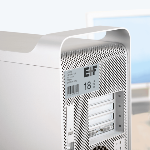 Silberner Computer mit perforierter Rückseite, ausgestattet mit mehreren Steckplätzen und technischen Spezifikationen auf einem Aufkleber.