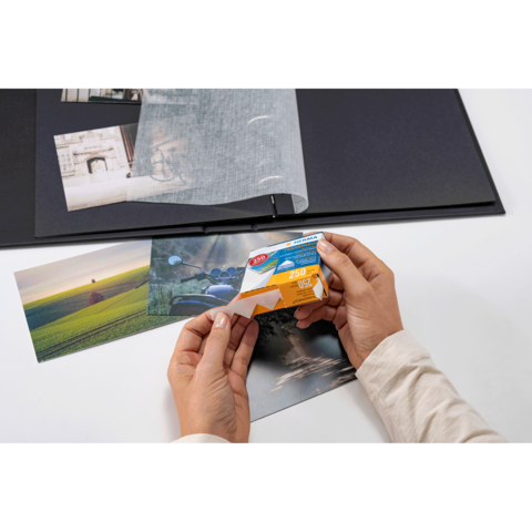 Eine Person hält eine Packung Fotopapier in der Hand, während sie Fotos in einem Album betrachtet.