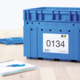 Blaue Kunststoffbox mit einer Etikette, die die Nummer 0134 und weitere Details zeigt, neben einem Notizblock und einem Stift.