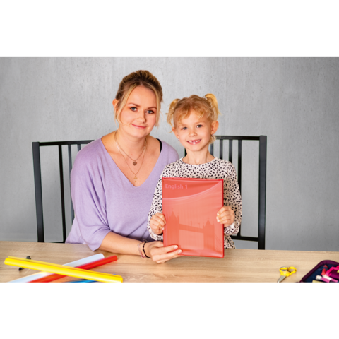 Eine Frau und ein kleines Mädchen sitzen an einem Tisch und halten ein rotes Heft mit der Aufschrift "English". Bunte Bastelmaterialien liegen auf dem Tisch.