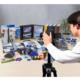Eine Person fotografiert verschiedene Büroartikel und Präsentationsmaterialien, die auf einem Tisch angeordnet sind. Im Hintergrund sind einige Ordner und eine Pflanze sichtbar.