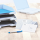 Ordner mit beschrifteten Fächern für eingehende und ausgehende Dokumente, dazu Briefe und ein blauer Stift auf einem Tisch.