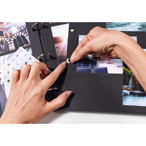 Eine Hand platziert einen Klebepunkt auf einer Seite eines Fotoalbums, das mit verschiedenen Bildern und Designs gefüllt ist.