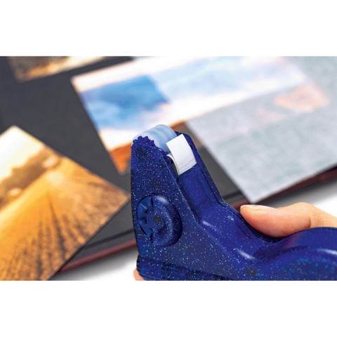 Eine Hand hält einen blauen Klebestift, während Fotos in einem Album angeordnet werden.
