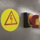 Warnschild mit Blitzsymbol und Not-Aus-Schalter an einer Wand.