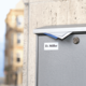 Graue Briefkasten mit dem Namen "D. Miller" auf einem urbanen Hintergrund, leicht nass von Regen.