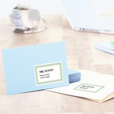 Ein blauer Umschlag mit der Aufschrift „MR. SUNNY“ und einer Adresse, neben einem weißen Umschlag und einem Laptop auf einem Holztisch.