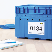 Blaue Kunststoffbox mit der Aufschrift "0134" und einem Etikett. Daneben ein Notizblock und ein blauer Stift auf einem Holztisch.