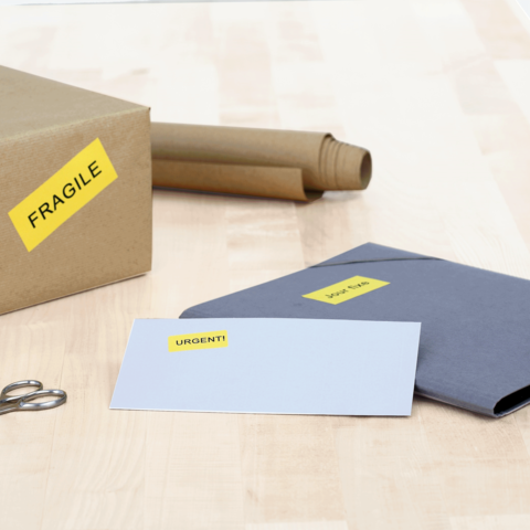 Ein brauner Karton mit dem Aufkleber "FRAGILE", daneben ein graues Kuvert mit dem Aufkleber "URGENT!" und eine Schere.