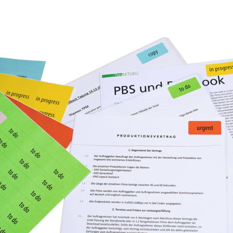 Vari documenti e appunti con post-it colorati, tra cui un contratto di produzione e un documento di lavoro su PBS e Facebook.