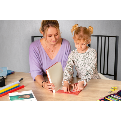 Eine Frau und ein Kind arbeiten gemeinsam an einem Bastelprojekt am Tisch, umgeben von Bastelmaterialien und Büchern.