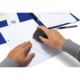 Eine Hand hält ein spezielles Gerät, das auf ein Blatt Papier gleitet, während eine andere Hand das Papier stabilisiert.