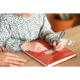 Ein Kind schreibt mit einem Stift in ein Buch, während eine Hand im Vordergrund Unterstützung bietet.