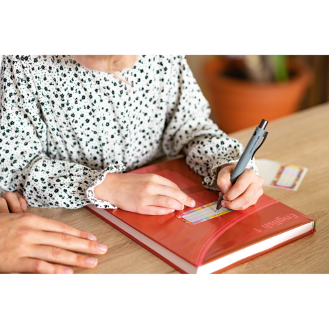 Ein Kind schreibt mit einem Stift in ein Buch, während eine Hand im Vordergrund Unterstützung bietet.
