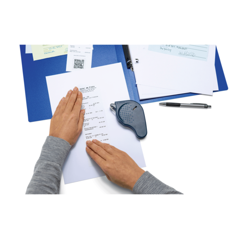 Eine Hand hält ein Blatt Papier mit Text, während ein Lesegerät daneben liegt. Im Hintergrund sind ein Ordner und ein Stift sichtbar.