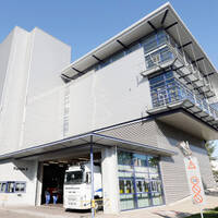 Moderne Lagerhalle mit Lkw im Eingangsbereich und großen Fenstern. Die Fassade ist aus Metall und hat mehrere Etagen.
