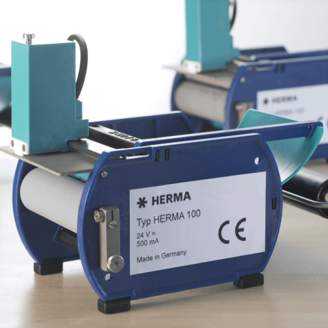 Gerät vom Typ HERMA 100, 24 V, 500 mA, hergestellt in Deutschland, mit blauer und grauer Gehäusefarbe.