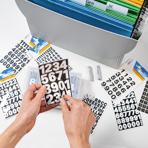 Eine Person hält ein Blatt mit bunten Aufklebern über einem geöffneten Planer, während sie Notizen macht.