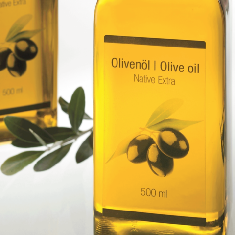 Flasche mit Olivenöl, 500 ml, beschriftet mit "Olivenöl | Olive oil" und "Native Extra", umgeben von Olivenzweigen.