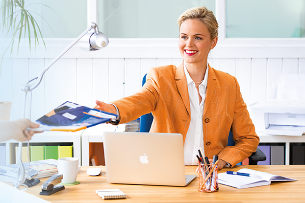 Due persone a un tavolo che presentano etichette. A sinistra un uomo con fogli di etichette, a destra una donna con un laptop e delle etichette.