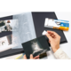 Eine Person hält eine Fotografie in der Hand, während sie ein Fotoalbum mit weiteren Bildern und einer Packung Fotohüllen betrachtet.
