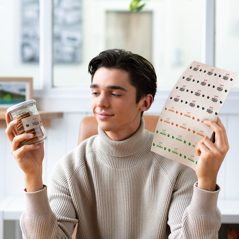 Un giovane tiene un bicchiere con snack in una mano e un'etichetta con diversi design nell'altra.